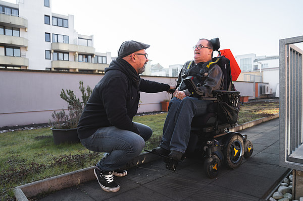 An emplyeee of supported living squats in front of a person in a wheelchair.